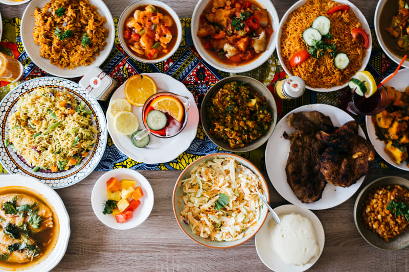 Bàn ăn minh họa ẩm thực Mali với nhiều đĩa cơm, thịt nướng, món hầm và rau củ