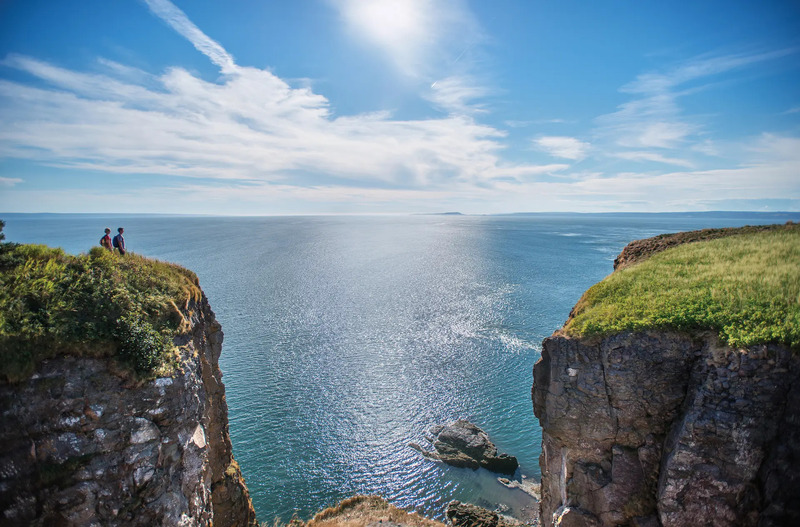 Hai vách đá phủ cỏ nhìn ra biển Nova Scotia dưới bầu trời xanh có mây trắng