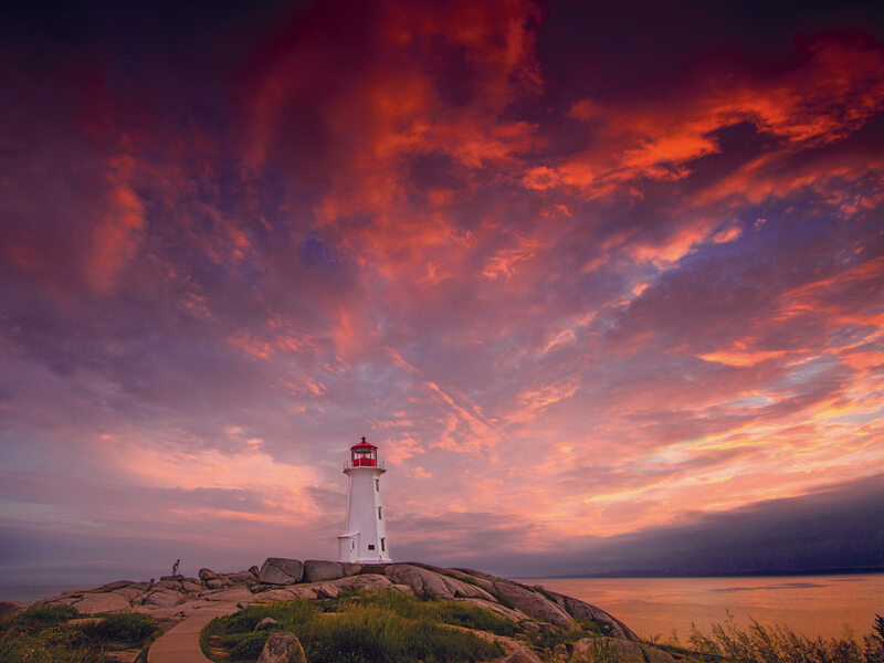 Hải đăng Peggy’s Cove ở Nova Scotia đứng trên bãi đá dưới bầu trời hoàng hôn đỏ cam