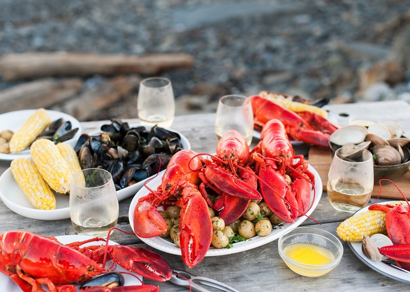 Bữa tiệc hải sản Nova Scotia với tôm hùm đỏ, vẹm, ngô và các món ăn kèm trên bàn ven biển